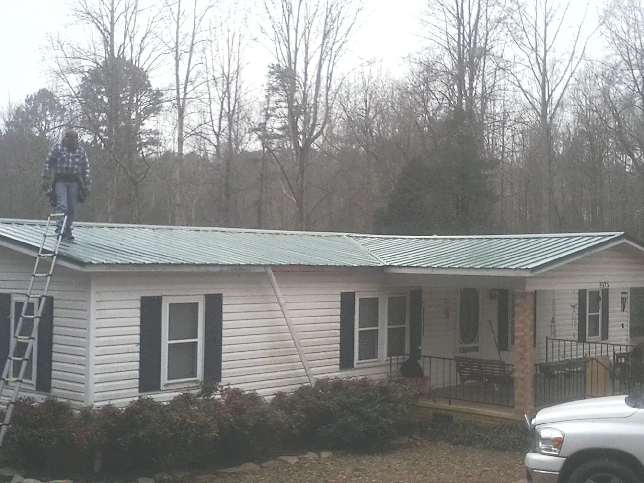 Worker on a ladder beside a new green metal roof on a ranch home in Union City